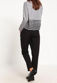 Maglietta grigia a maniche lunghe con un motivo nero testurizzato nella parte inferiore, abbinata a pantaloni neri a sigaretta e scarpe nere.