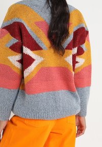 Pull tricoté coloré avec un motif géométrique en rouge, jaune, bleu et rose. Texture douce avec une coupe décontractée et un ourlet côtelé.