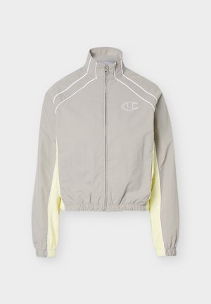 Lysegrå jakke med lynlås, høj krave, gule sidepaneler, elastiske manchetter og kant samt et lille hvidt logo på brystet.