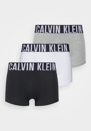Drie paar boxershorts in zwart, grijs en wit, met een brede zwarte tailleband waarop in witte letters "CALVIN KLEIN" staat gedrukt.