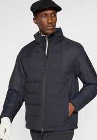 Casaco de puffer azul marinho com fecho de zipper, seções acolchoadas e gola alta. Inclui bolsos laterais e painéis texturizados nas mangas.