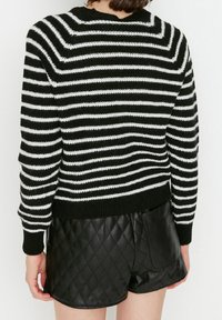 Schwarz-weiß gestreifter Strickpullover mit rundem Ausschnitt und geripptem Saum, kombiniert mit schwarzen, gesteppten Leder-Shorts.