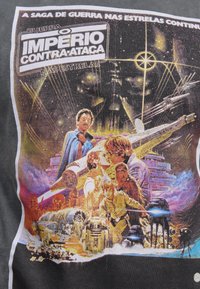 Grafisk T-shirt med en färgglad illustration från "Star Wars: The Empire Strikes Back", som visar karaktärer och rymdskepp mot en stjärnig bakgrund.