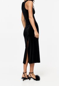 Robe midi en velours noir à coupe ajustée, avec des fentes latérales. Associée à des sandales noires à lanières ornées d'un accent duveteux sur les orteils.