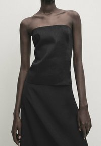 Black strapless top made of smooth fabric, featuring a straight neckline and a fitted design, paired with a matching black skirt.