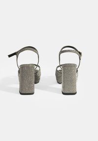Hakken sandalen met een glinsterende zilveren textuur, open achterkant, enkelbandje en chunky platform hak ontwerp. Zwarte zool.