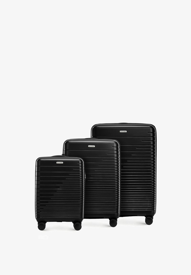 Trois valises noires rigides de tailles variées. Elles présentent une texture rayée, quatre roues et des poignées supérieures pour une maniabilité facile.