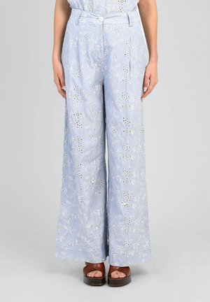 Pantalon large bleu clair avec broderie florale blanche, fermeture à boutons, porté avec des sandales compensées marron et un chemisier assorti rentré.