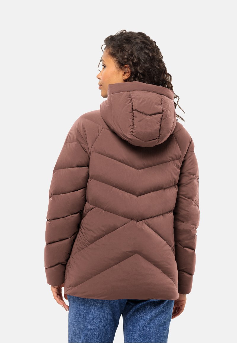 Braune Pufferjacke mit Kapuze, ausgestattet mit einem Zickzack-Steppmuster und gerippten Bündchen. Getragen über blauen Denim-Jeans.
