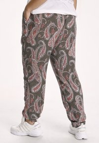 Pantalon imprimé avec une base marron ornée de motifs cachemire en rouge, blanc et bleu. Le tissu offre une texture douce. Ourlets ajustables aux chevilles.