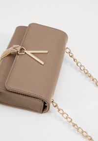 Bolso de mano de imitación cuero marrón con textura, con una correa de cadena dorada, que presenta un tirador de cremallera dorado y forma rectangular. Cierre en la parte superior.