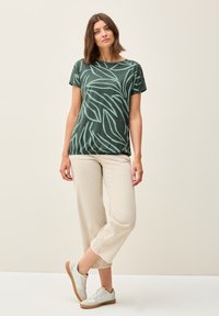 Camiseta verde con patrón de hojas, cuello redondo, mangas cortas, combinada con pantalones cortos de color crema y zapatillas ligeras. Conjunto simple y casual.