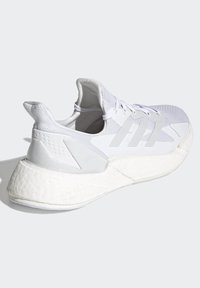 Chaussure de sport blanche avec une tige en mesh texturé, un design à trois bandes, une semelle intermédiaire rembourrée et une semelle extérieure en caoutchouc épais distinctive.