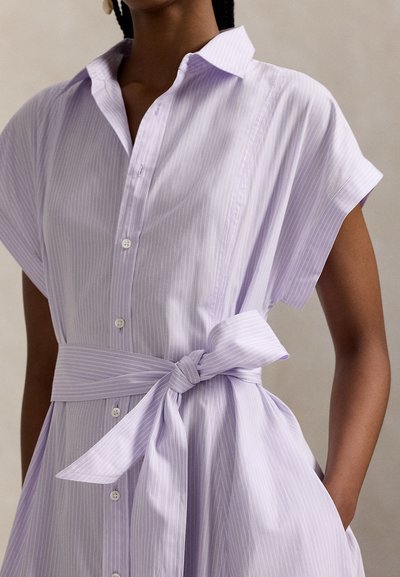 Φόρεμα πουκάμισο με λωρίδες σε χρώμα λεβάντας, κοντά μανίκια, κουμπιά στο μπροστινό μέρος και ζώνη στη μέση που δένει. Λείο ύφασμα με κάθετες γραμμές και διακριτική υφή.