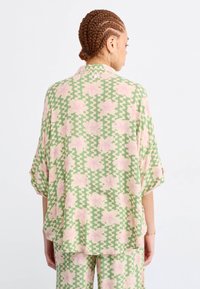 Lichte, losse blouse met een groen en roze bloempatroon en een zigzagdesign. Voorzien van korte mouwen en een kraag.