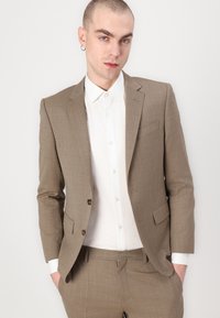 Giacca a quadri marrone con design strutturato, due bottoni e una camicia bianca sotto. Vestibilità slim con finitura in tessuto testurizzato.