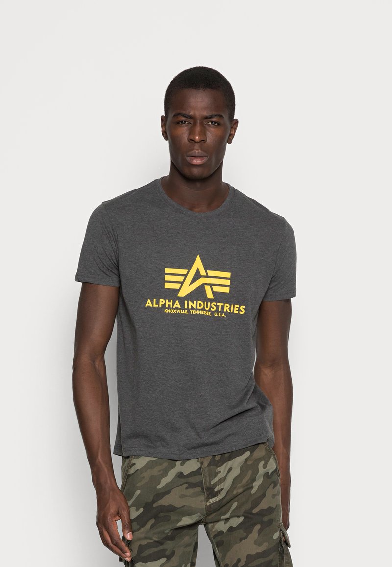 Grey cotton t-shirt with a round neckline and short sleeves featuring a yellow "ALPHA INDUSTRIES" logo and triangular design at the chest.