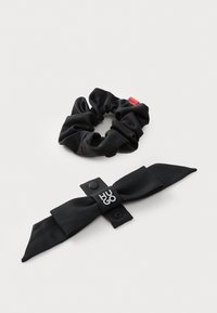 Kaks musta juukseaksessuaari: sileda viimistlusega scrunchie ja nööbiga sulgumisega ning logo aktsendiga lipsu peapael.