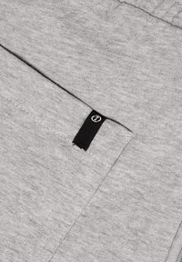 Grauer Sweatshirtstoff mit strukturierter Oberfläche, ausgestattet mit einem schwarzen Etikett. Das Design umfasst eine Tasche und einen einfachen, klaren Schnitt.