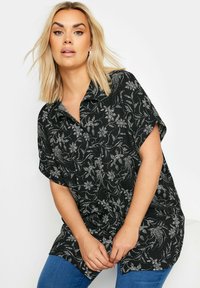 Camicia nera a maniche corte con un motivo floreale bianco, colletto e vestibilità rilassata, realizzata in tessuto testurizzato.