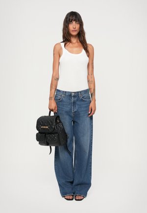 Weißes Tanktop, lockere blaue Jeans, schwarzer gesteppter Rucksack mit Trägern und schwarze offene Absatzschuhe. Einfaches und funktionales Design.
