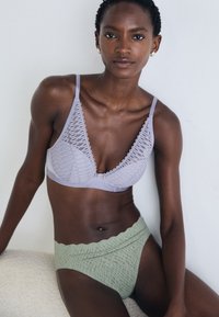 Απαλή λευκή δαντελένια τοπ με V κοπή, σε συνδυασμό με υφασμάτινα πράσινα σλιπ ψηλής μέσης που διαθέτουν κυματιστό λάστιχο στη μέση.