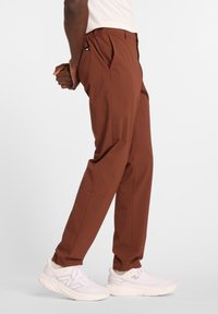 Pantaloni marroni a vestibilità rilassata, con pieghe frontali e vita elastica, abbinati a scarpe sportive bianche.