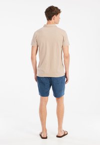 Korte mouw beige polo shirt gecombineerd met blauwe corduroy shorts. De stof lijkt zacht, met een relaxed fit en een subtiele textuur.