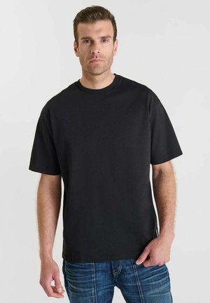 Camiseta negra de manga corta hecha de algodón, con un clásico cuello redondo y un corte relajado. Textura suave sin patrones visibles.