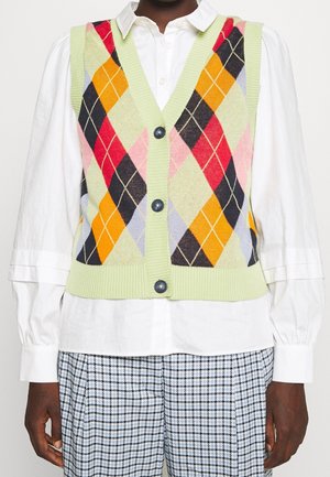 Ärmellose grüne Argyle-Strickweste mit orangefarbenen, roten, schwarzen und rosa Rauten, getragen über einem weißen Hemd mit Knöpfen und karierten Hosen.