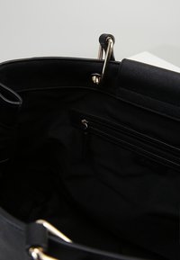 Svart väska med en slät yta, guldfärgad hårdvara och ett rymligt inre med en ficka med dragkedja mot en tygfoder.