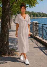 Woman in a white dress and white sneakers walking on a tree-lined waterfront path with railing and water beside it.