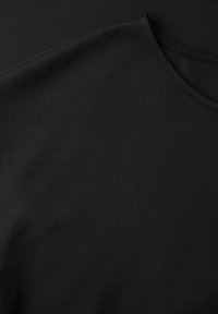 Černé tričko s kulatým výstřihem, detail látky ukazující hladkou texturu a detaily švů kolem výstřihu a ramene.