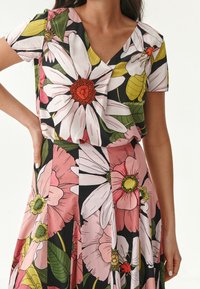 Blomstret kjole med V-hals, korte ærmer, sort baggrund, store pink og hvide blomstermønstre, grønne blade og plisseret skørt design.