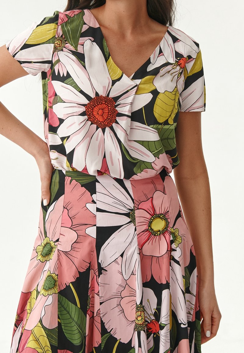 Blomstret kjole med V-hals, korte ærmer, sort baggrund, store pink og hvide blomstermønstre, grønne blade og plisseret skørt design.