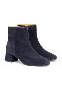 Botas de tobillo de ante azul marino con tacón cuadrado, punta afilada y cierre de cremallera. La suela presenta un detalle rojo en la base del tacón.