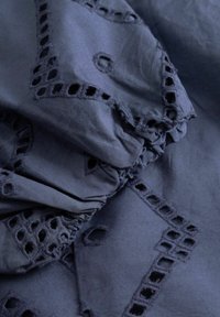 Donkerblauwe stof met vierkante en ronde uitsnede borduurwerk en geplooide elastische details.