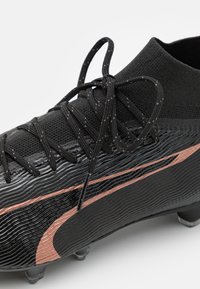 Scarpini da calcio neri con un design testurizzato, dettagli in oro rosa e un colletto lavorato a maglia con lacci neri per un'aderenza sicura.
