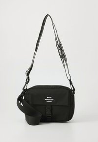 Bolsa de mensajero negra con correa ajustable, que presenta una tela lisa, forma rectangular, solapa frontal y logo blanco impreso.