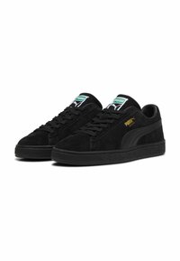 Sneakers nere in suede con suola in gomma, dotate di etichetta verde e bianca sulla linguetta e marchio "Puma" dorato di lato.