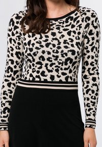 Långärmad leopardmönstrad topp i beige och svart, med en figurnära design och en kontrasterande randig midja. Slät stickad textur.