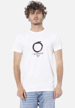 T-shirt di cotone bianco con un logo circolare nero, accentuato da un nastro e il testo "TRUSSARDI Milano 1911" sottostante, vestibilità casual, maniche corte.