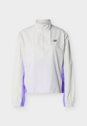 Biely športový bomber s celým zipsom, vysokým golierom, elastickými manžetami, fialovými bočnými panelmi a čiernym logom New Balance na hrudi.