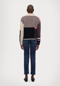Gebreide trui met hoge kraag, voorzien van een patchworkontwerp in verschillende kleuren, gecombineerd met donkerblauwe skinny jeans en zwarte ballerina's.