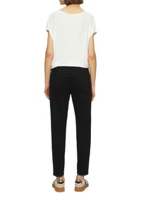 Haut blanc à manches courtes associé à un pantalon noir cintré et des chaussures avec des accents métalliques. La tenue présente un design simple et décontracté.