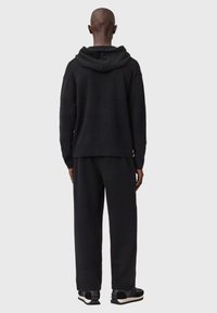 Schwarzer Strick-Hoodie mit lockerem Schnitt, ausgestattet mit Kapuze und langen Ärmeln. Kombiniert mit passenden schwarzen Jogginghosen und Sportschuhen.