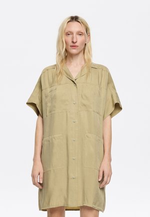 Vestito camicia a maniche corte in khaki chiaro, realizzato in tessuto morbido. Presenta due grandi tasche frontali e chiusura con bottoni sul davanti.