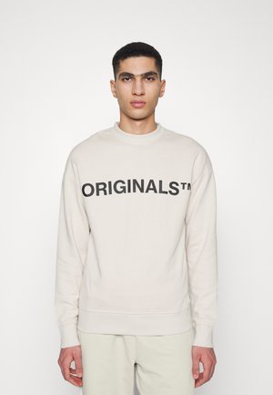 Light beige sweatshirt made of soft fabric, featuring a round neck and long sleeves. Bold black text "ORIGINALS™" across the front.