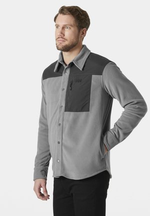 Grijze fleece shirtjack met een contrasterend zwart bovenstuk en zak. Voorzien van drukknoopsluiting en een kraag.