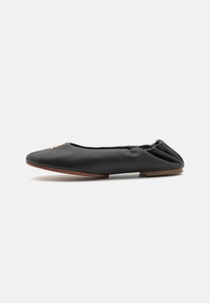 Chaussure plate en cuir noir avec un bout pointu et un design minimaliste. Présente un petit accent décoratif à l'avant et un petit talon.